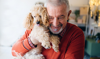 Senior man smiles while hugging his pet dog inside home.