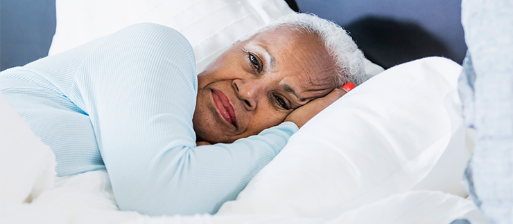 Senior woman lays on her side in bed trying to fall asleep.