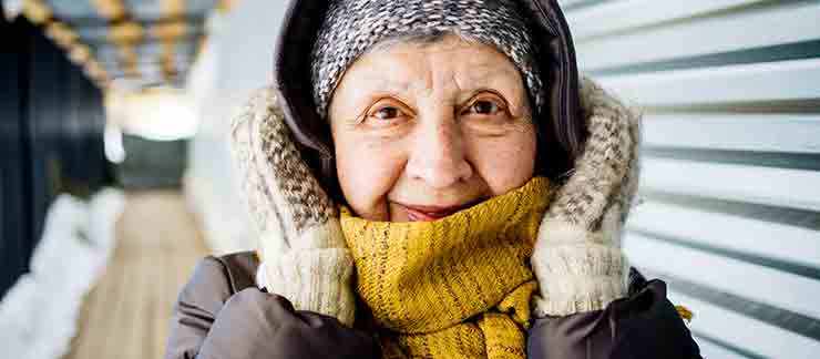 Elderly woman wearing a heavy coat, scarf, hat, and mittens on a cold, winter day.