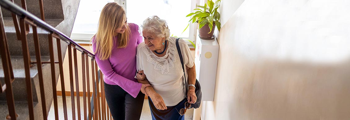 Female caregiver helps an elderly woman up the stairs to prevent a fall or accident.