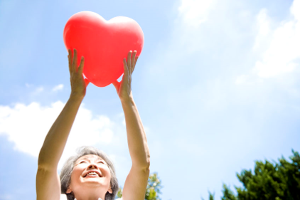 Elderly woman holding up heart decoration in the air