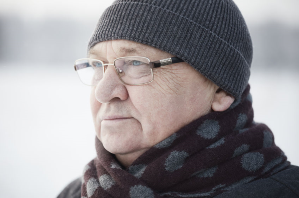 Elderly man standing outside wearing winter hat with coat