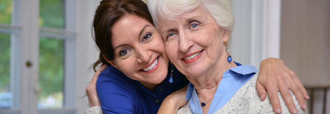 In-home companion care worker hugs senior woman.