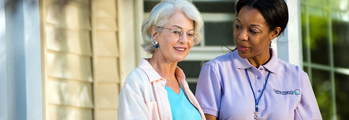 Professional home care worker provides walking assistance to elderly woman outside.