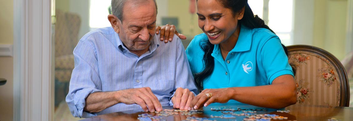Visiting Angels' female caregiver happily works on a puzzle with elderly man.
