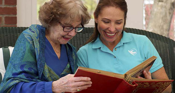 Female home care worker looks through old photo album with senior woman at home.