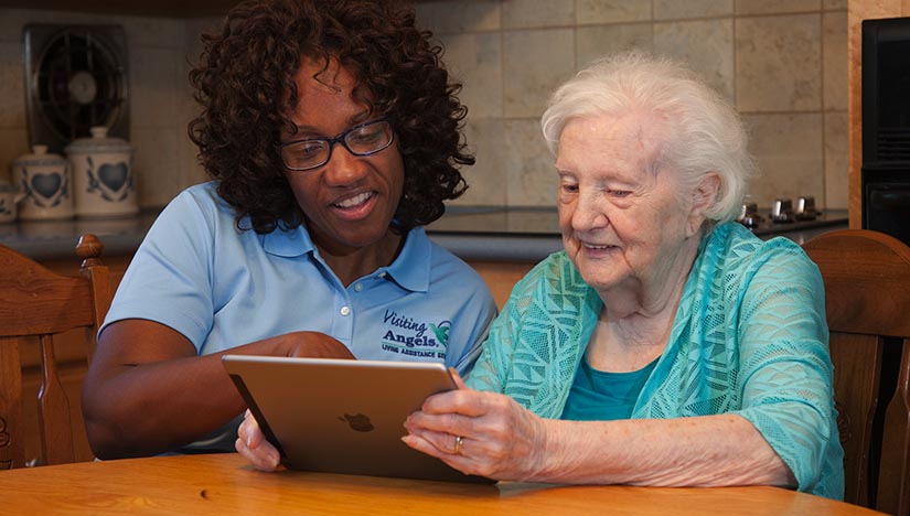At-home care provider from Visiting Angels Littleton teaching senior woman how to use an iPad