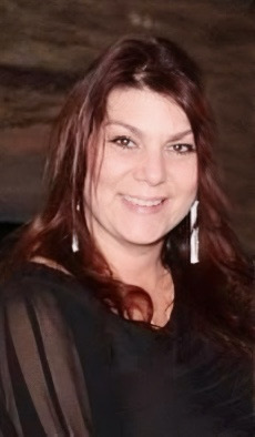 Woman with red hair and long silver earrings wearing a black dress smiling at the camera