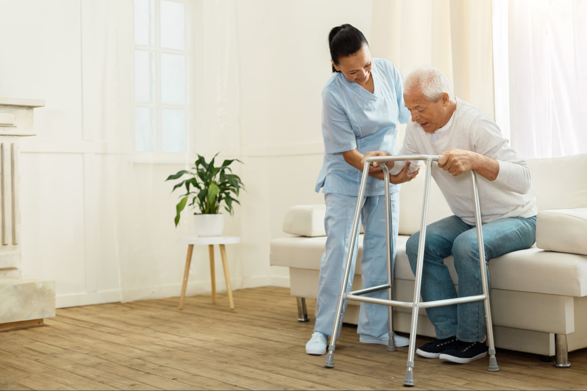Nurse helping older man off couch and to a walker