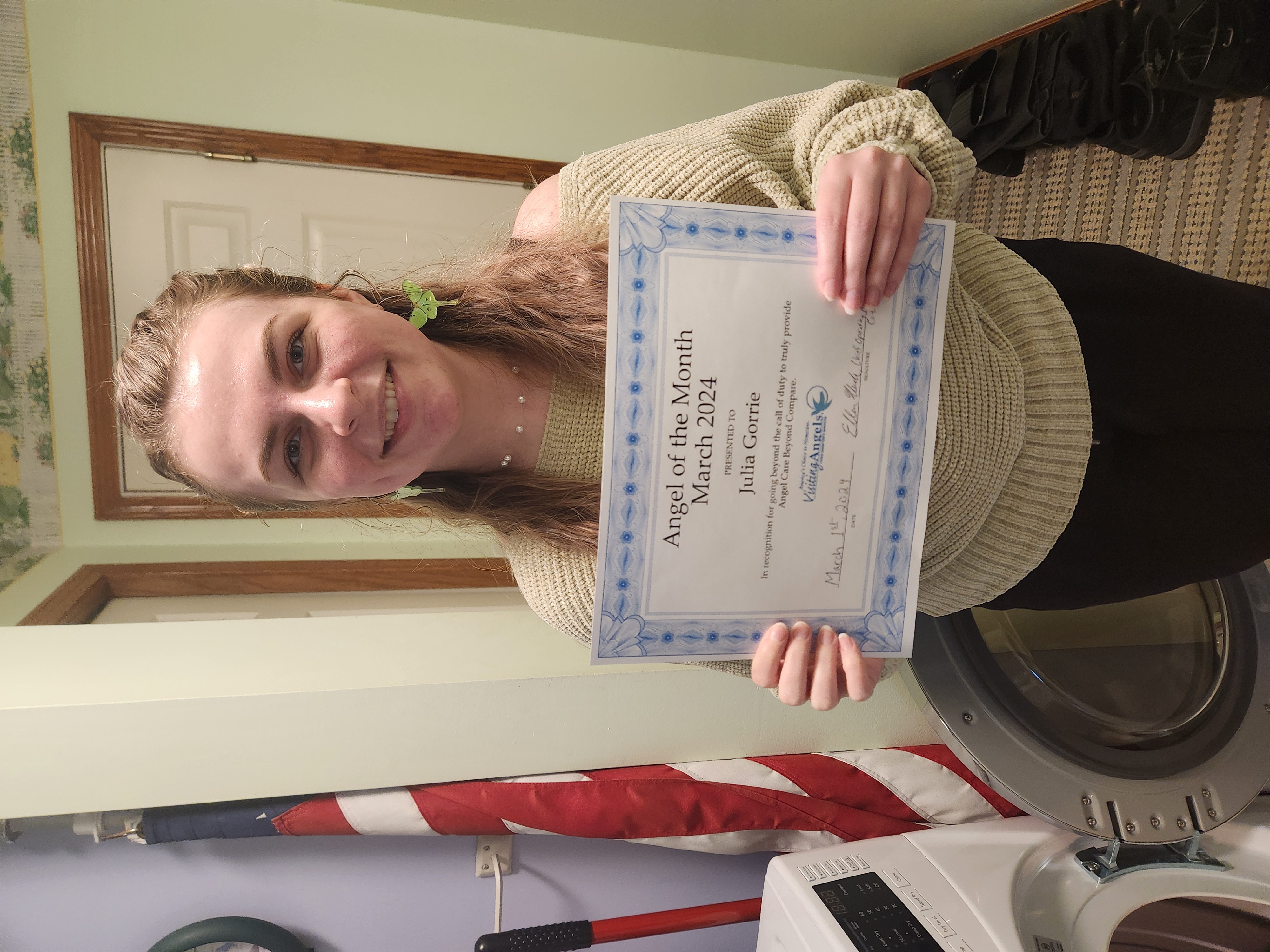 Julia Gorrie smiles and shows her printed award for Angel of the Month for excellent caregiving in home care to clients in Allegan, Kalamazoo, Mattawan, Paw Paw, Plainwell, Portage, and Southwest Michigan.