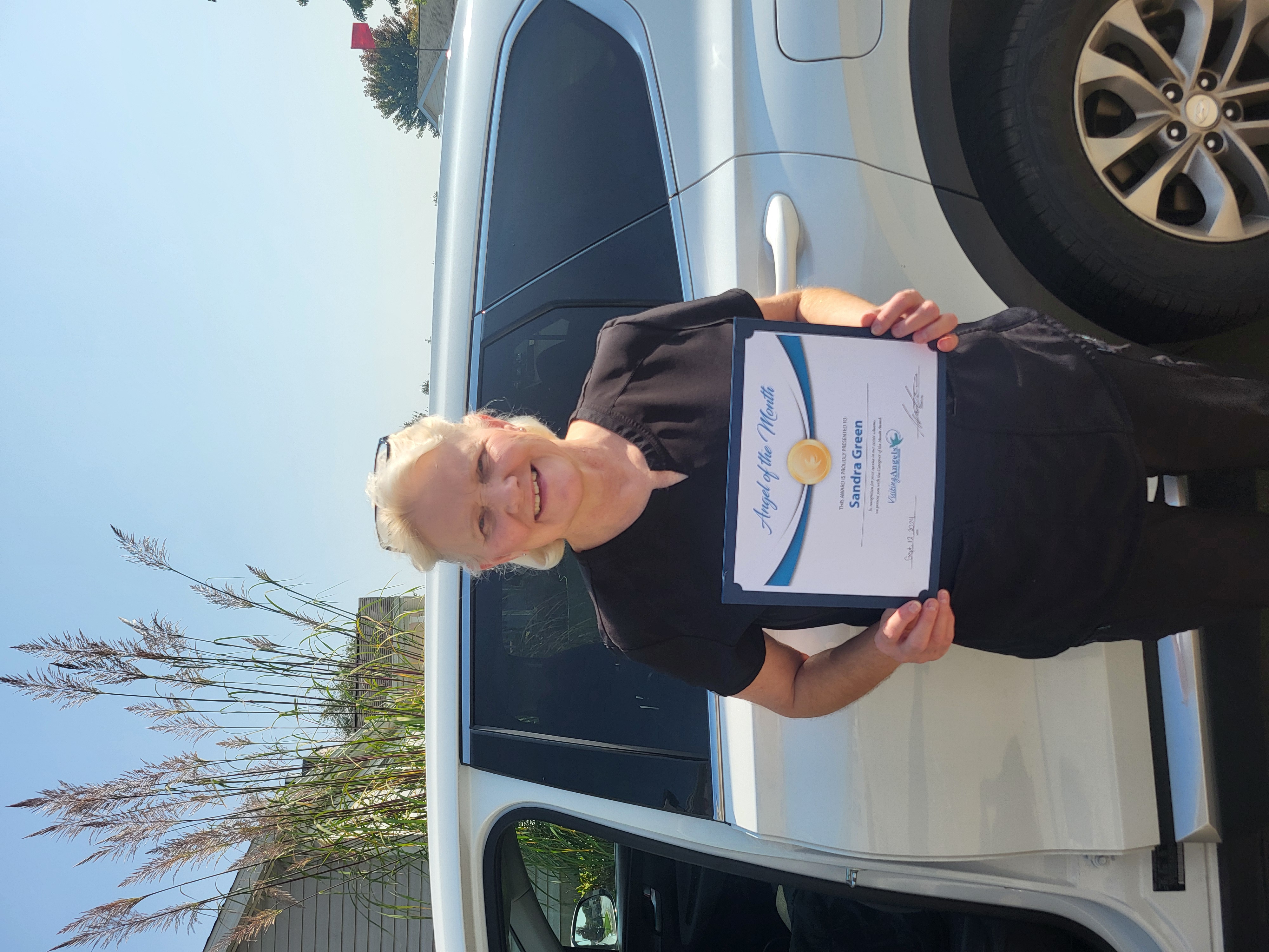 Sandra Green smiles and shows her printed award for Angel of the Month for excellent caregiving in home care to clients in Allegan, Kalamazoo, Mattawan, Paw Paw, Plainwell, Portage, and Southwest Michigan.