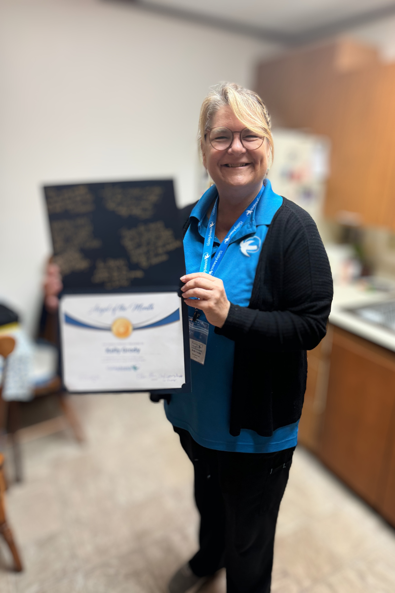 Kelly Grody smiles and shows her printed award for Angel of the Month for October 2024 for excellent caregiving in home care to clients in Allegan, Kalamazoo, Mattawan, Paw Paw, Plainwell, Portage, and Southwest Michigan.