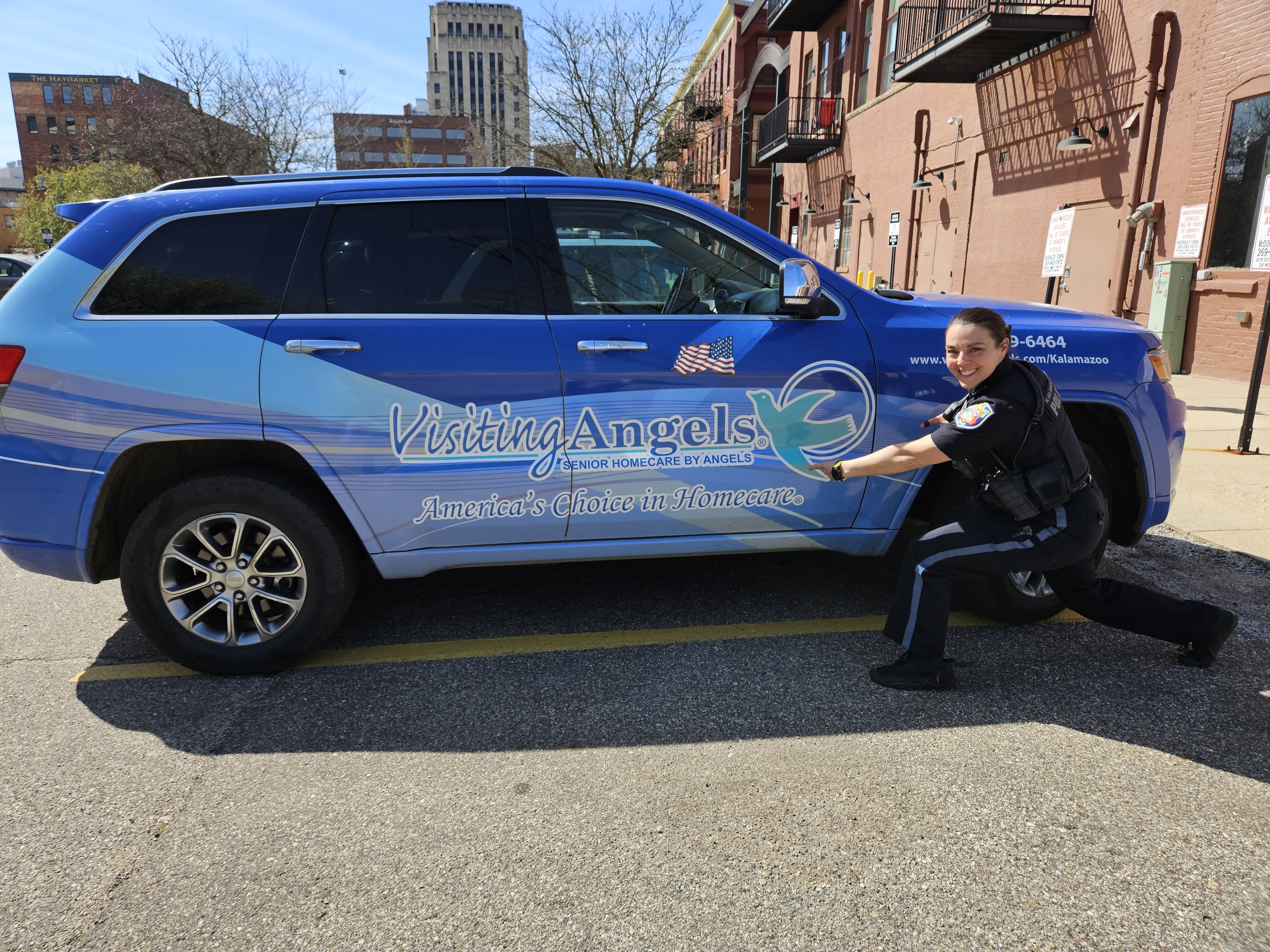 A Kalamazoo Department of Public Safety Officer playfully points at the Visiting Angels of Southwest Michigan van which is explicitly branded and parked in downtown Kalamazoo.