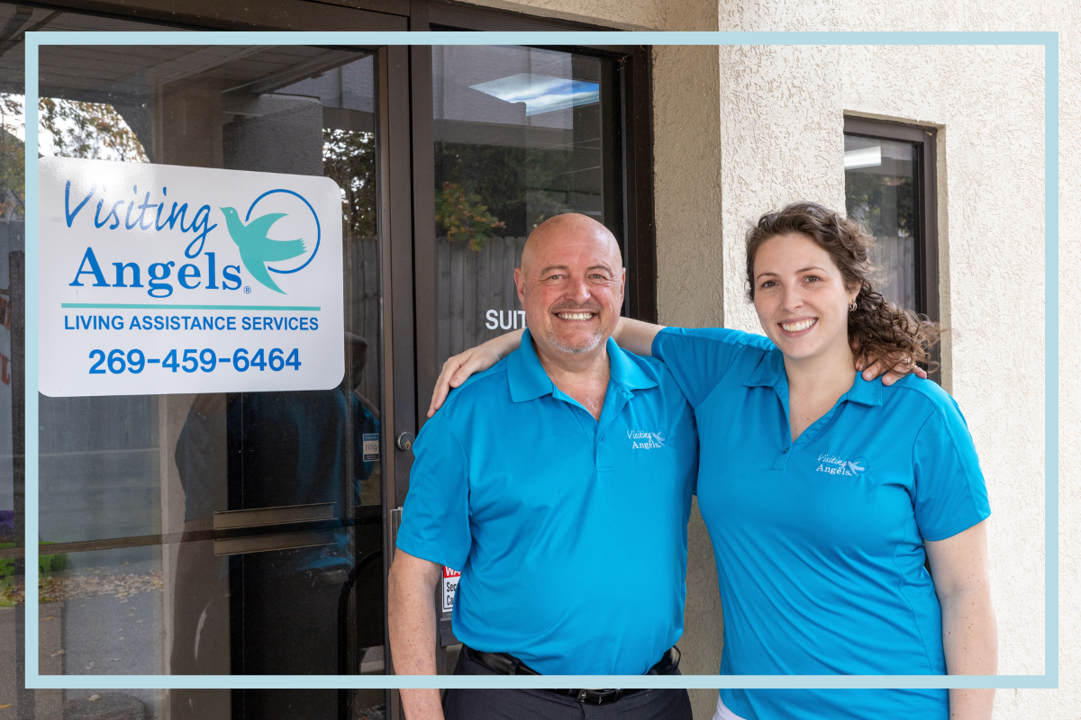 Founder Denny Stults smiles with his arm around daughter and current owner, Ellen Kluck. Both smile at the camera in front of the front door of the Portage Visiting Angels office, which displays the logo on the door.