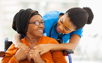 A caregiver giving an older woman a hug from behind.