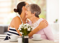 Younger woman hugging and elderly woman while sitting at a table.
