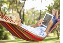 Senior woman resting on a hammock reading an iPad.